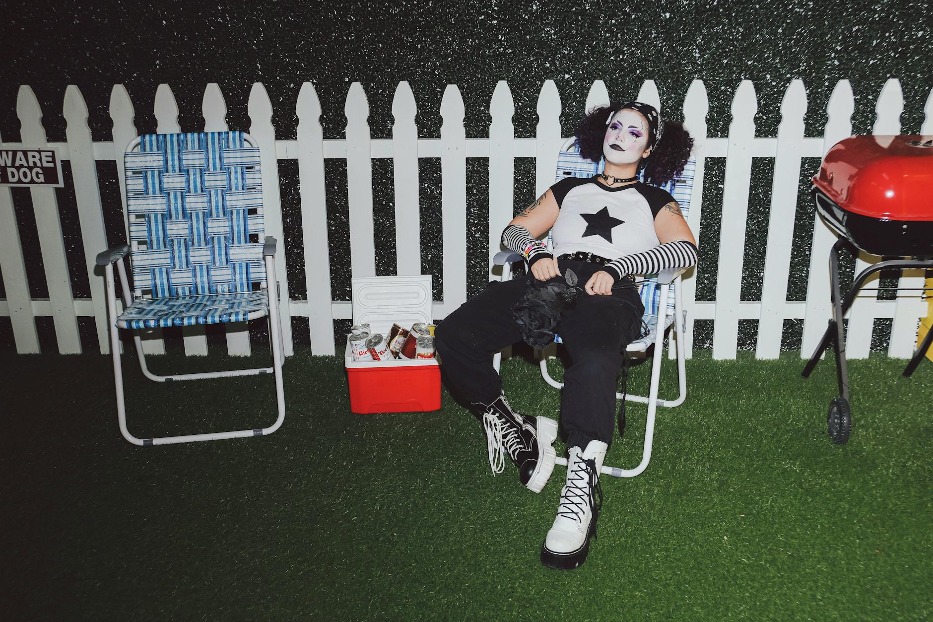 Osoba w gotyckim stroju siedzi nocą przy grillu w ogrodzie