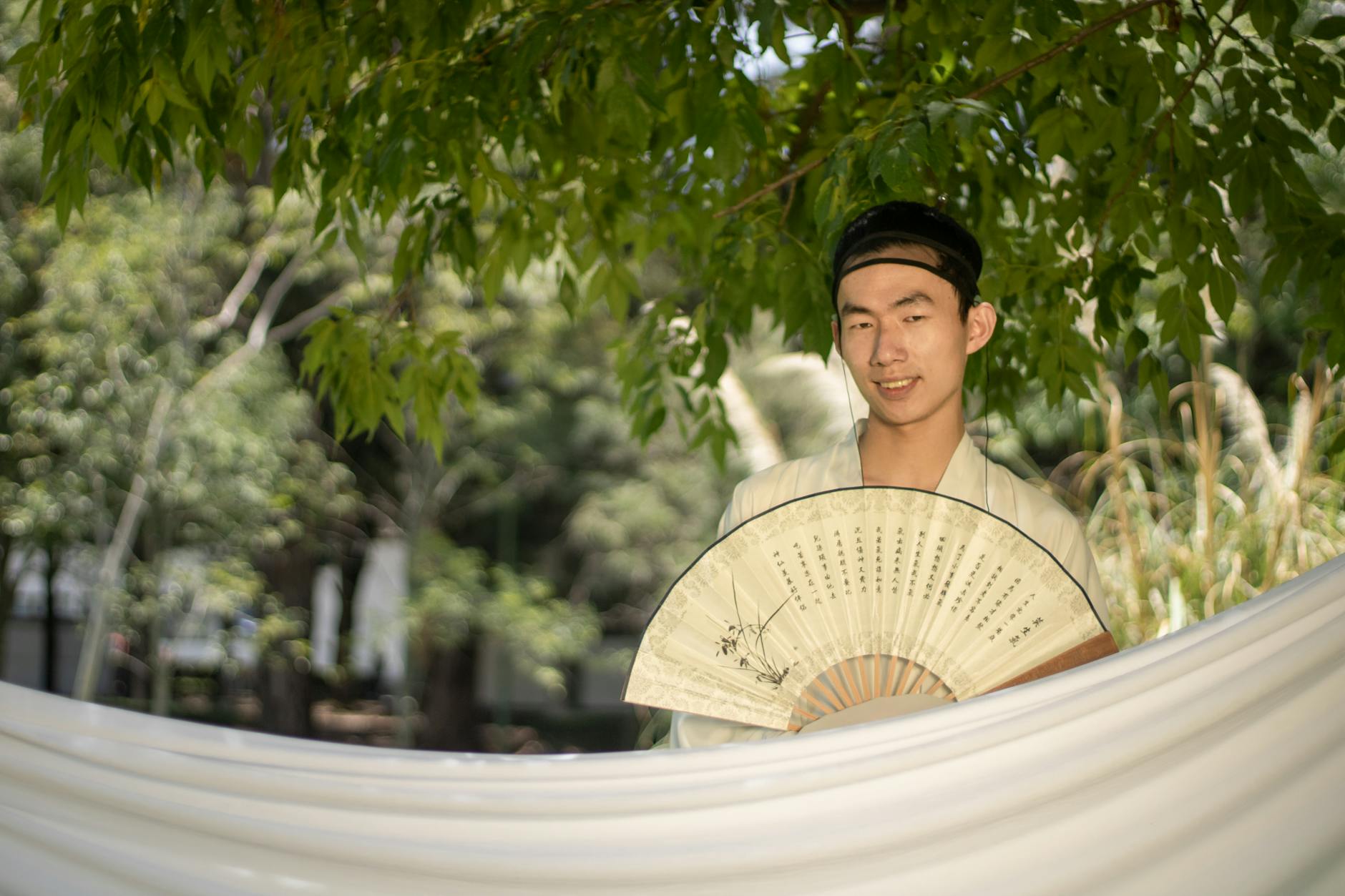 Mężczyzna w tradycyjnym stroju z wachlarzem w cieniu drzew w ogrodzie