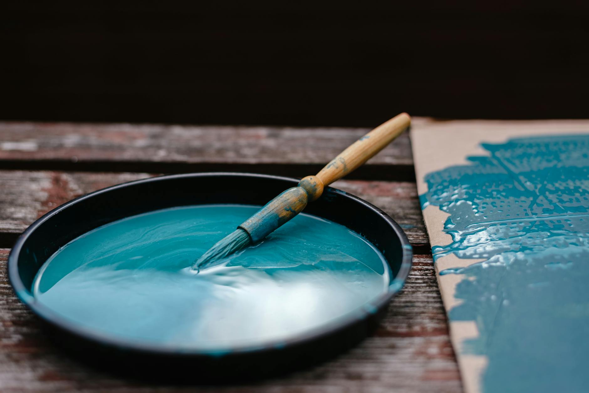 Pędzel w misce z niebieską farbą na drewnianej ławce ogrodowej