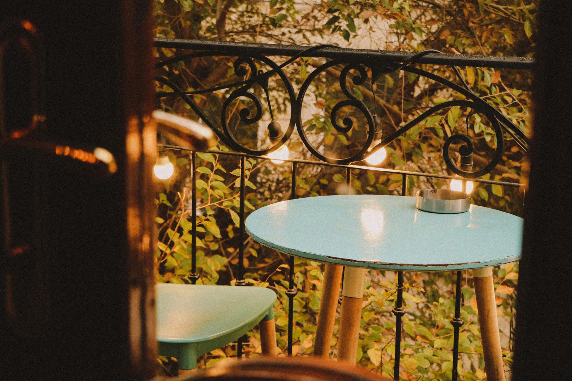Wieczorny balkon z niebieskim stolikiem, krzesłem i ciepłymi lampkami